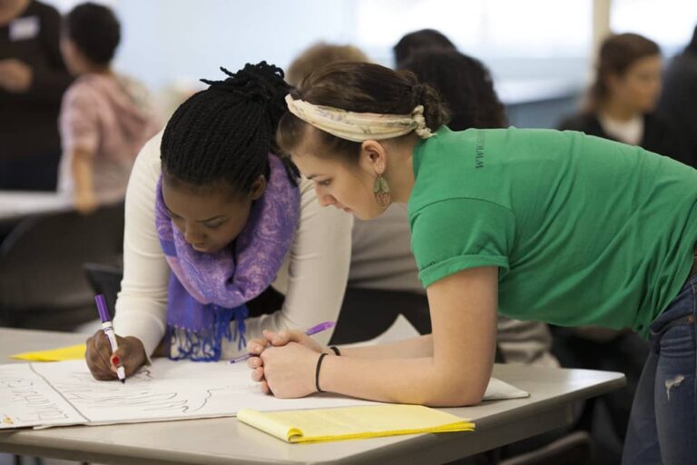 Two women collaborating on a project together in a classroom setting, focused and engaged in their work.